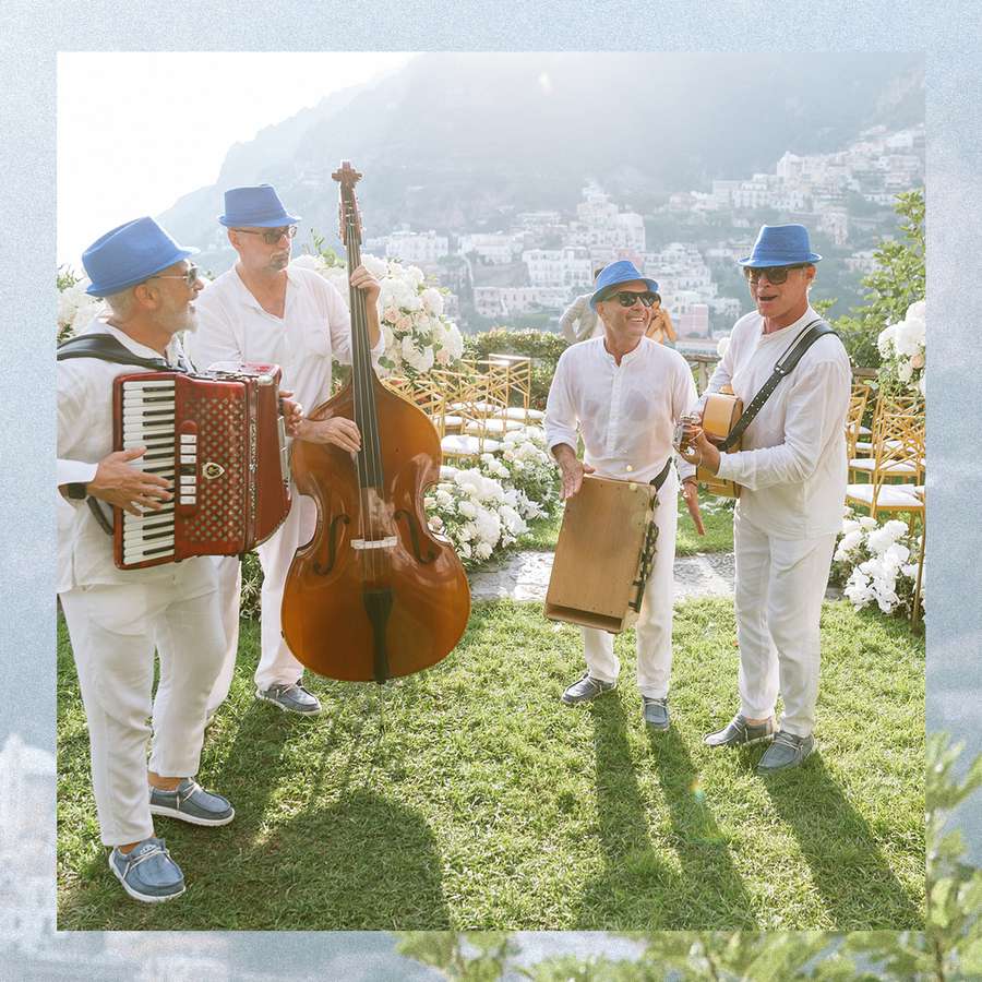 A five-piece band of men in white outfits with blue hats performs at an outdoor wedding.