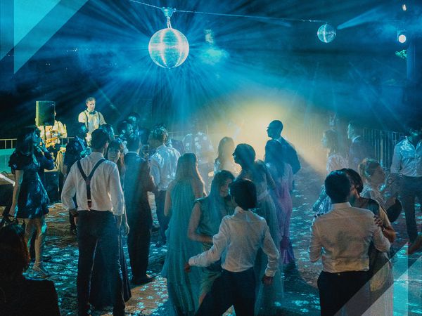 Wedding guests dance on a blue-lit dance floor below a disco ball.