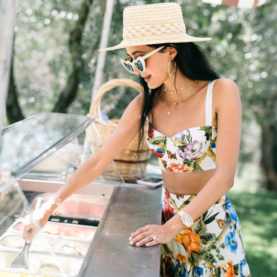 Girl in a sun hat, heart-shaped sunglasses, and floral top and skirt scooping at an ice cream/gelato bar