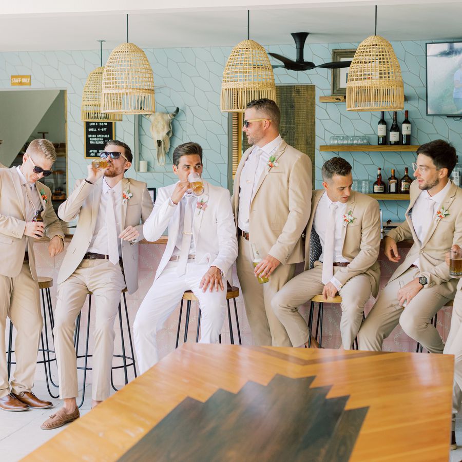 groom and groomsmen in tan suits sitting at a bar