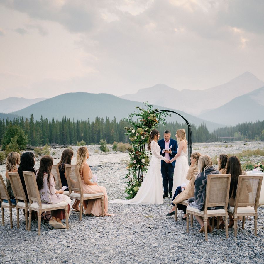 Two brides holding hands at the altar surrounded by a mountain landscape