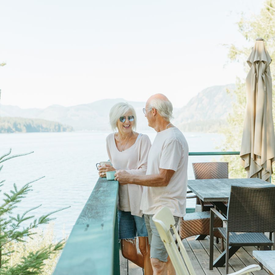 Older couple standing on a deck with a cups of coffee, with a lake and mountains in the background 