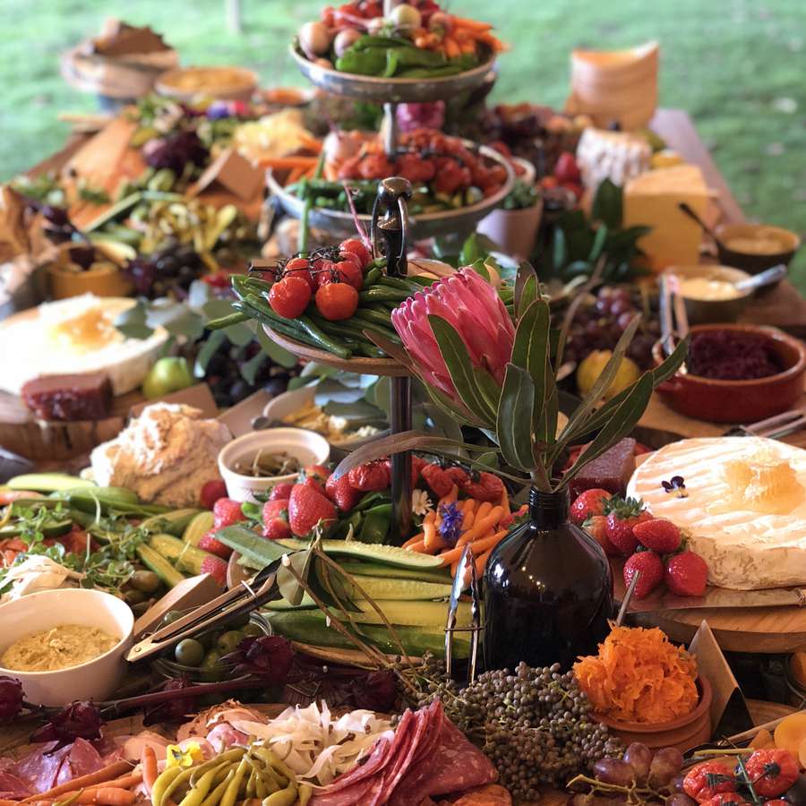 A spread of brie, tomatoes, string beans, strawberries, cucumbers, carrots, and other produce at an outdoor summer wedding