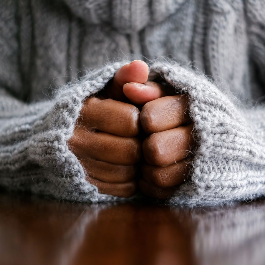 Close-up of a black woman wearing a sweater and clasping her hands in frustration.