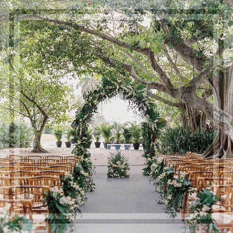 A wedding ceremony arch with greenery and wooden chairs for guest seating.