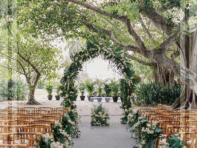 A wedding ceremony arch with greenery and wooden chairs for guest seating.