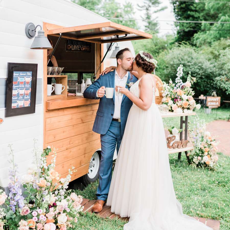 Bride and groom holding coffee mugs and kissing in front of a mobile coffee truck