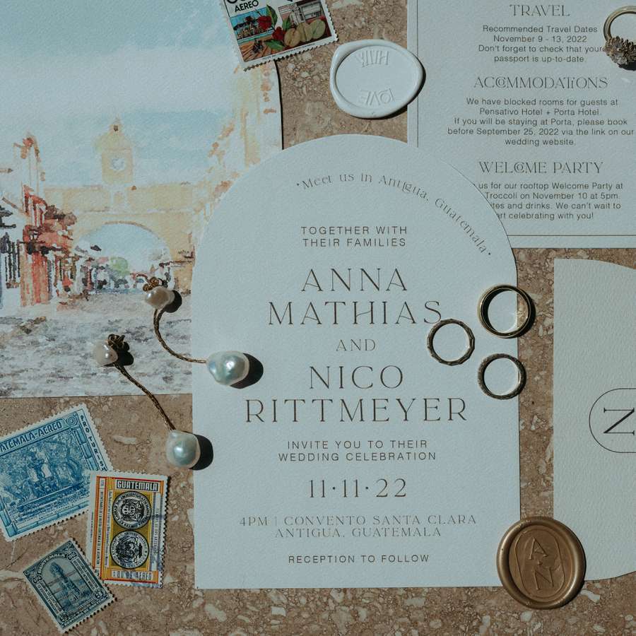 An arched invitation with an 11/11/22 wedding date in gold font surrounded by local stamps, a details card, and a venue illustration