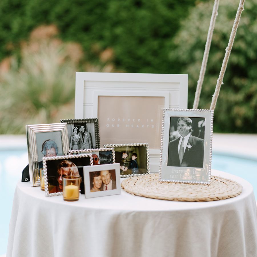 A memorial table at a wedding with framed photos of deceased loved ones, candles, and a wicker charger