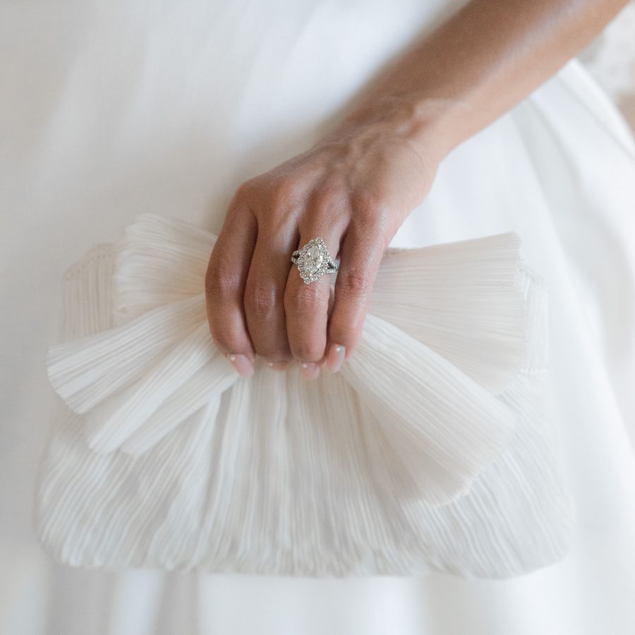 bride holding a white clutch wearing a marquise cut diamond engagement ring