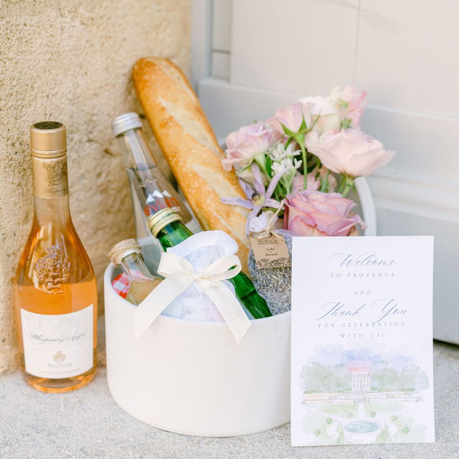 A welcome bag filled with flowers, sparkling water, local beverages, candies, a baguette, and a bottle of alcohol