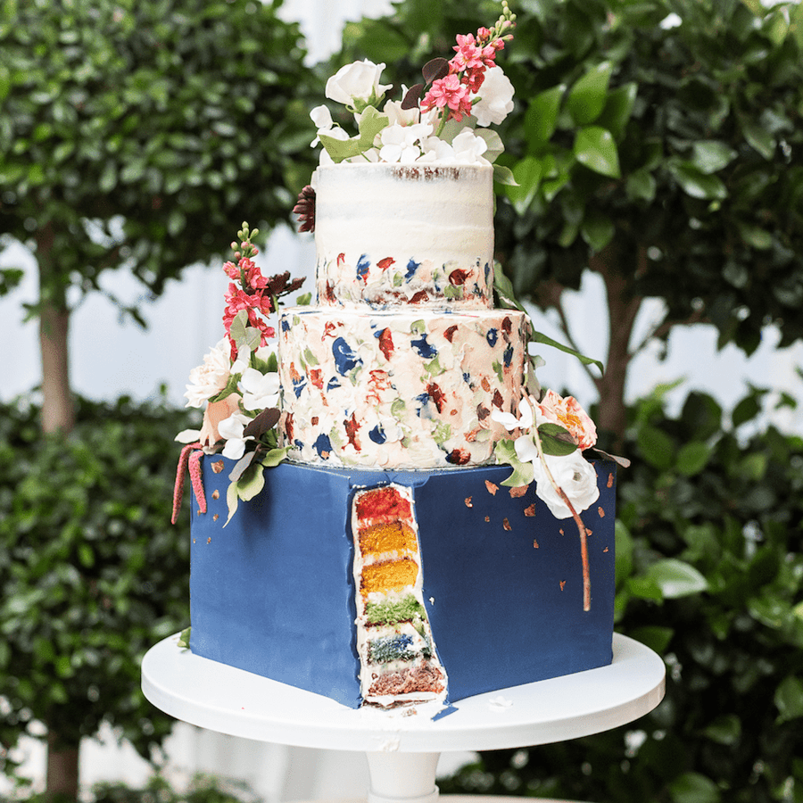 Three-tier wedding cake with rainbow cake filling topped with flowers